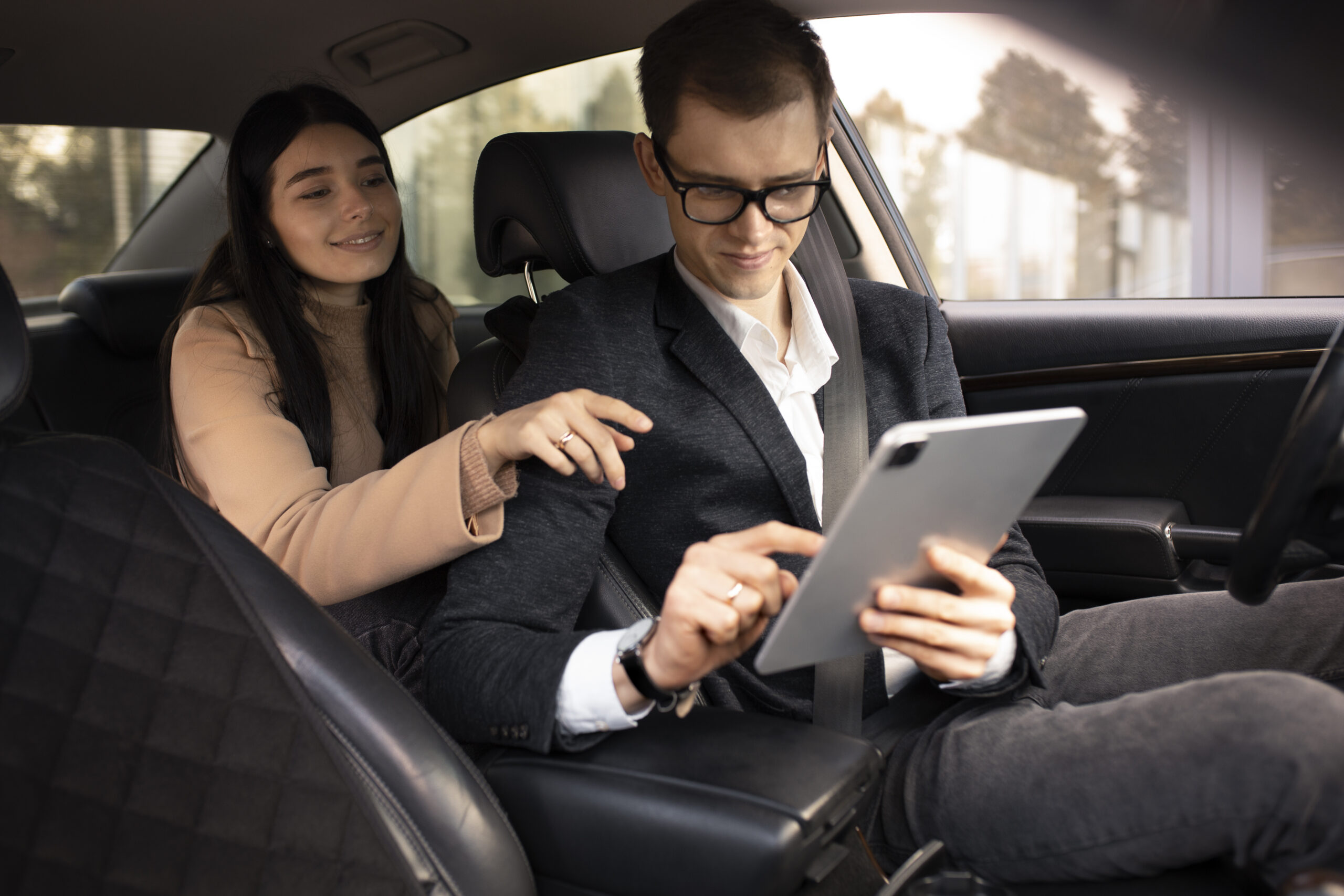 Business professionals in car reviewing tablet, showing cab rentals for meetings and conferences.